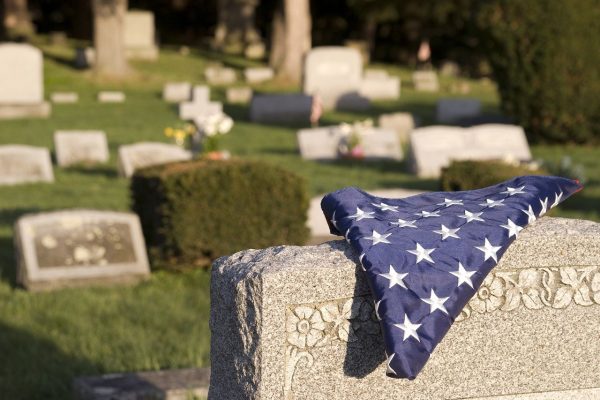 A folded American flag lays on top of a tombstone in a cemetery.