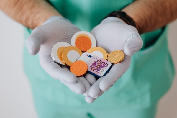 A medical professional in scrubs and gloves holds a handful of British coins.