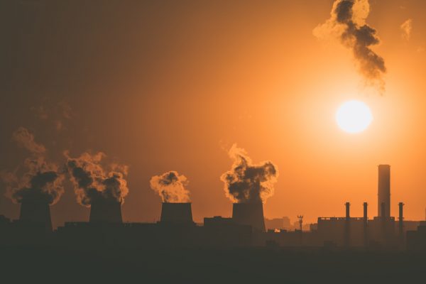 A factory emitting a smoke-like substance is silhouetted in a sunset.